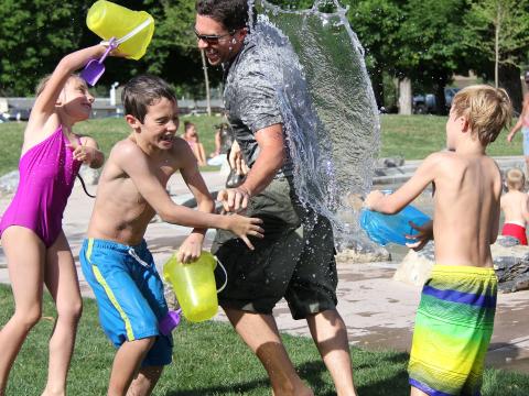 Drei Kinder spielen mit einem Erwachsenen mit Wasser